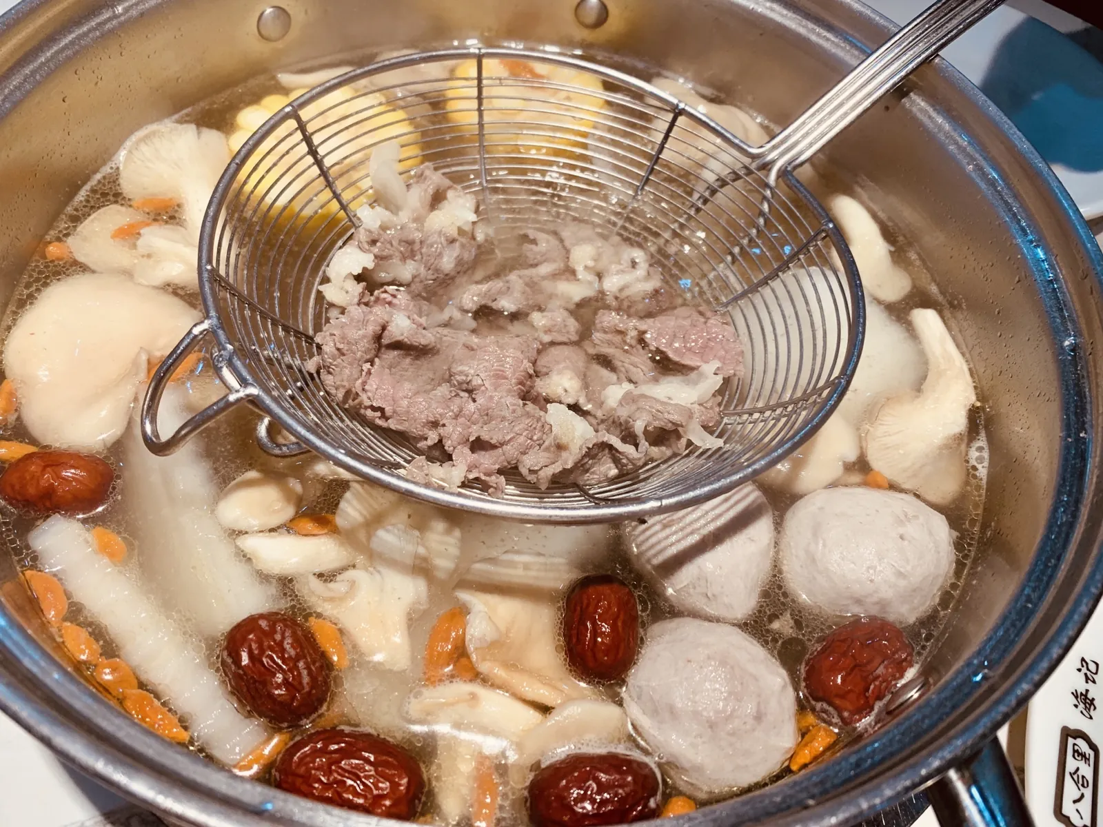 透き通った潮汕火鍋のスープで、牛肉丸と一緒に金属のざるで煮える薄切り牛肉