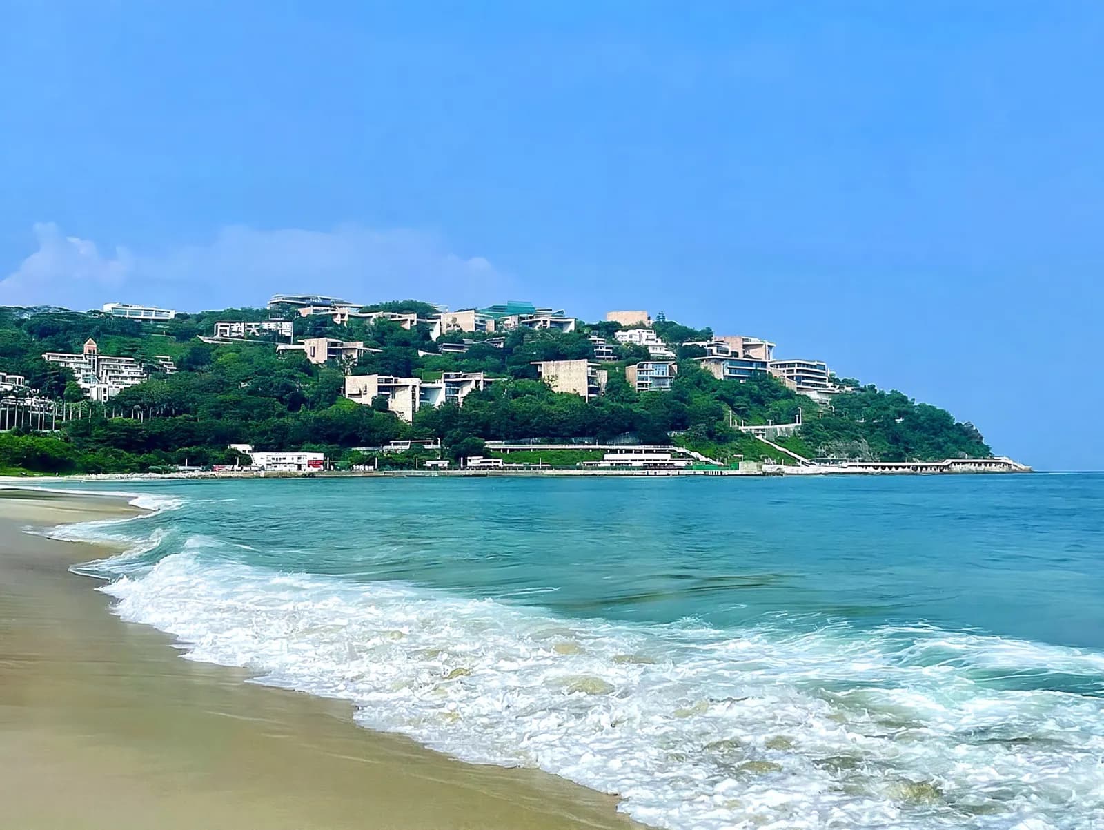 Waves breaking on Dameisha Beach with hillside villas behind