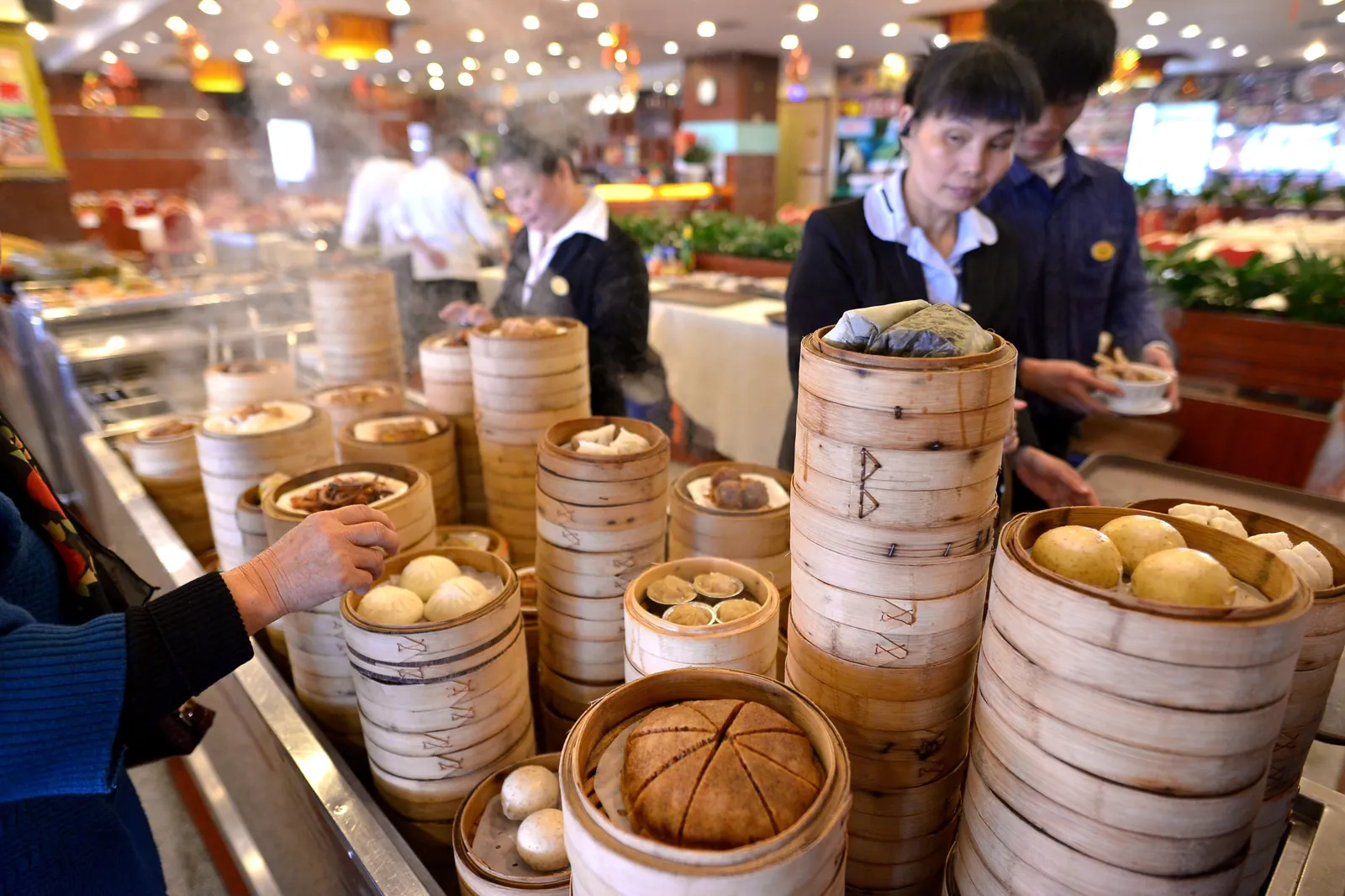 Stacked bamboo steamers at a teahouse counter with staff serving dim sum