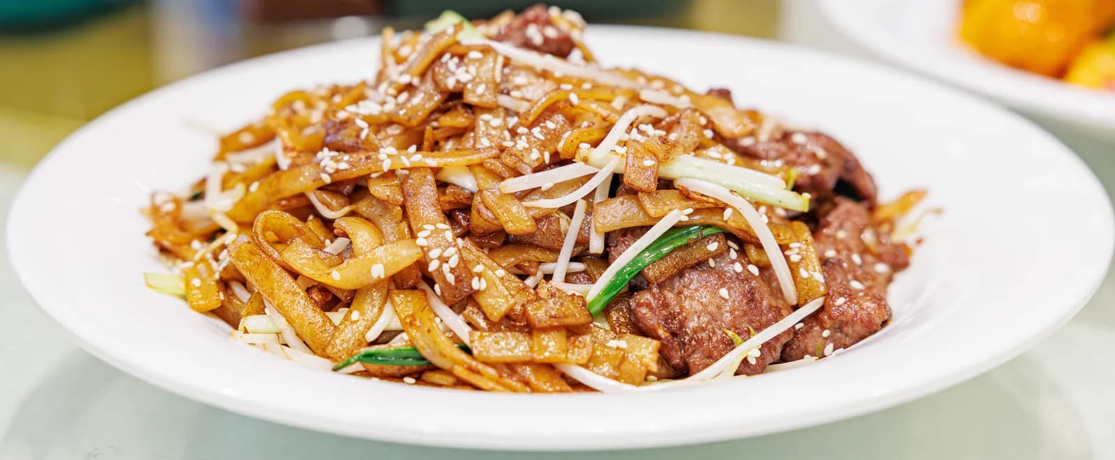 Plate of dry-fried beef ho fun with wide rice noodles, beef and bean sprouts