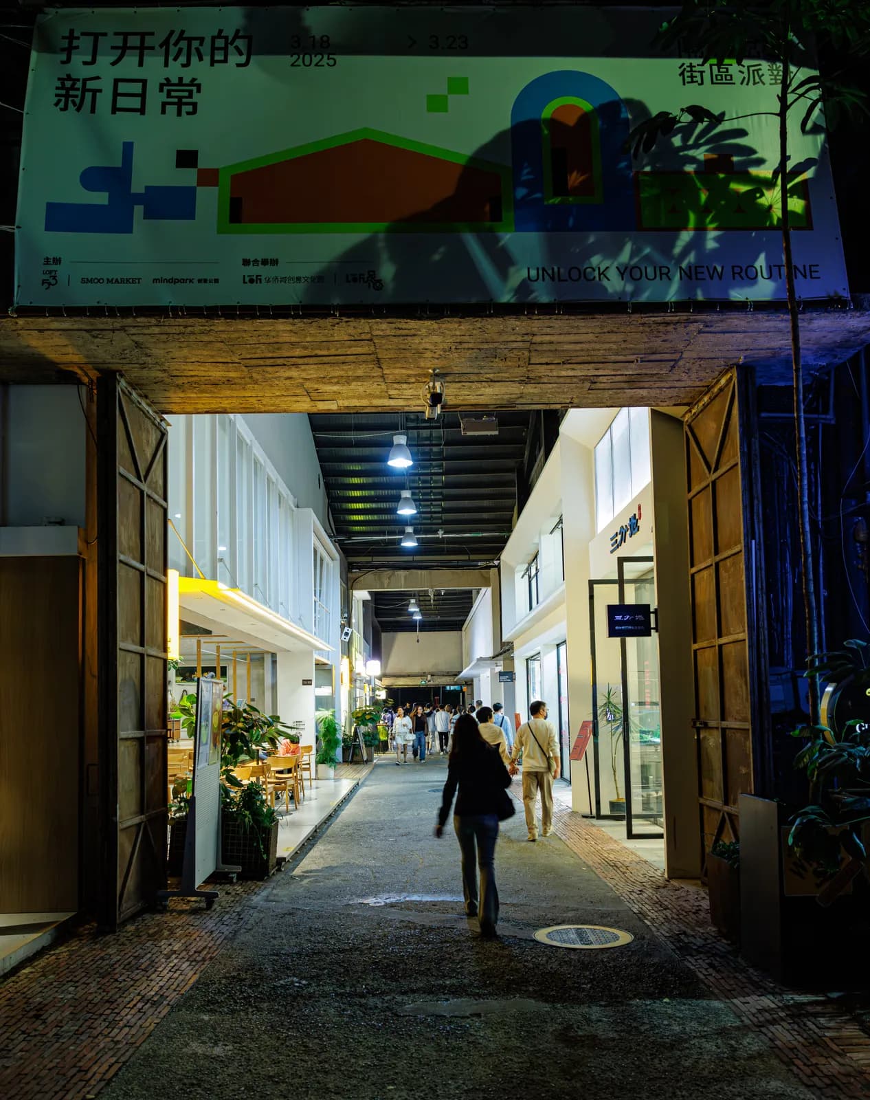 Covered passage under an OCT-LOFT market banner at night, with cafes and studios on both sides