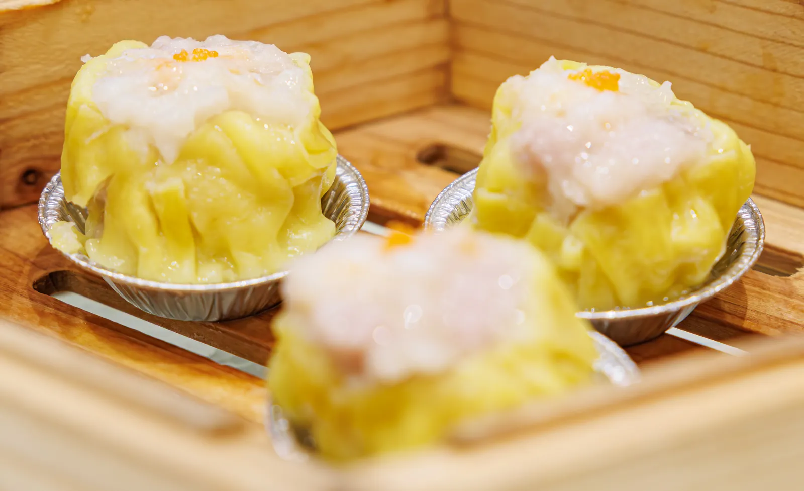 Yellow-wrapped siu mai pork and shrimp dumplings topped with roe in a steamer