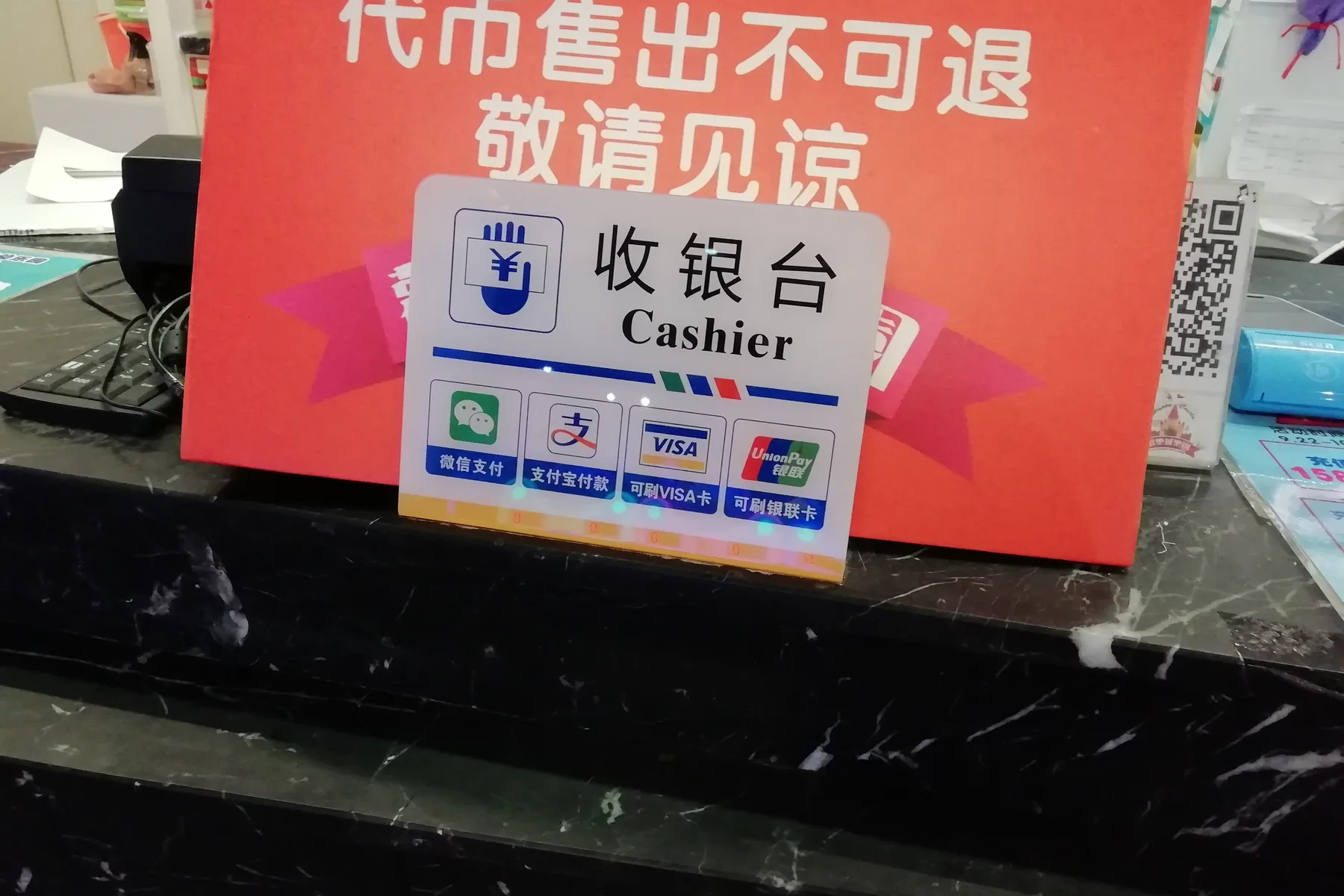 Cashier counter sign displaying WeChat Pay, Alipay, Visa, and UnionPay acceptance alongside a QR standee